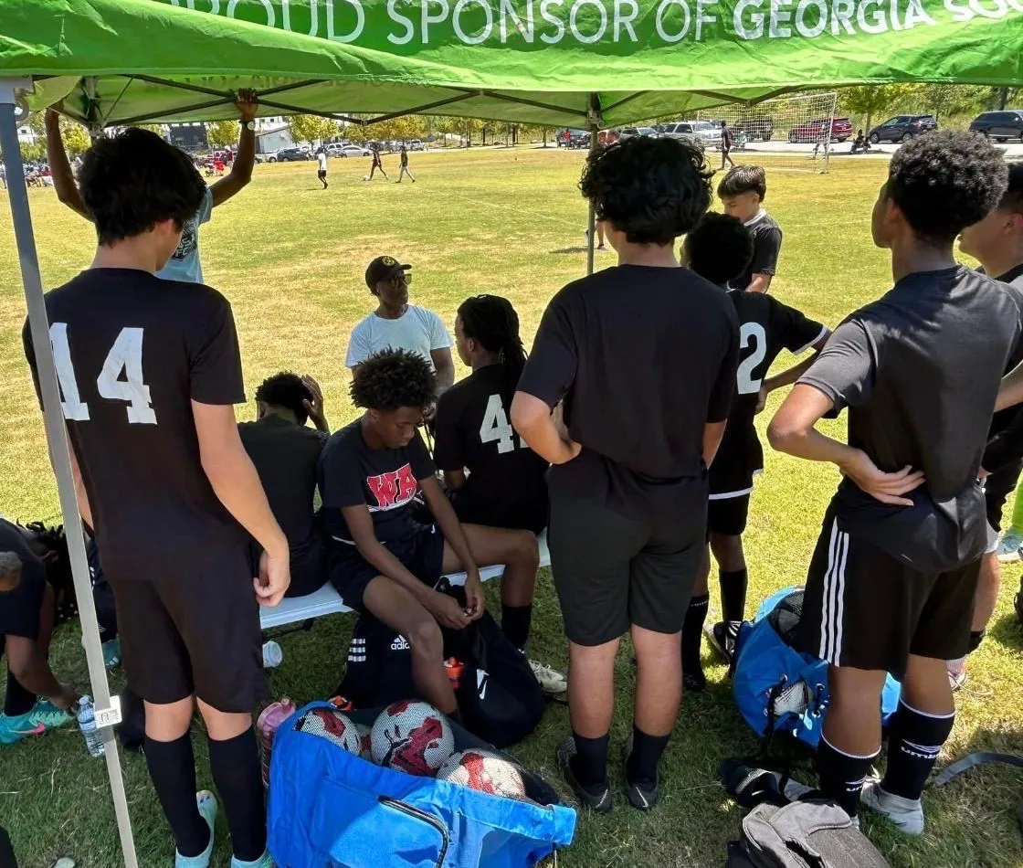 FitSquad boys’ soccer team meeting with their coach under a sponsor tent